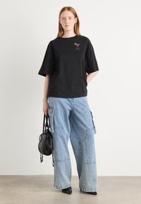 Black cotton t-shirt with short sleeves and a pink cocktail glass graphic. Paired with light blue wide-leg cargo jeans and a black handbag.