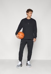 Sort atletisk langærmet skjorte med logo og matchende sweatpants, parret med en basketball og grå sneakers. Glat stofstruktur.