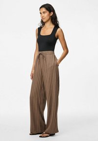 Svart ärmlös bodysuit som matchas med bruna, vida byxor med vertikala ränder, som har dragsko i midjan och en avslappnad passform.