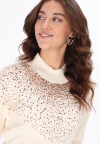 Suéter beige claro con cuello alto, adornado con lentejuelas en tonos rosa y marrón, con un diseño de punto texturizado.