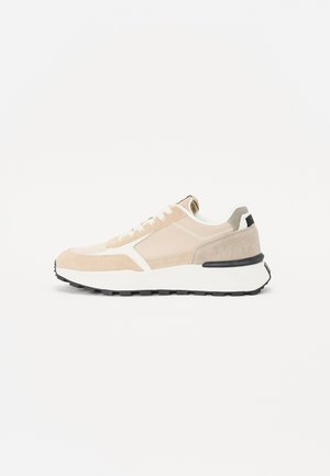 Beige and cream athletic sneakers with suede and mesh materials, lace-up closure, and black rubber sole, featuring a textured accent on the heel.