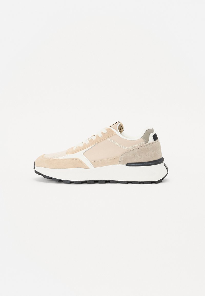 Beige og krem joggesko laget av semsket skinn og mesh-materiale, med snøring og svart gummisåle, som har en teksturert detalj på hælen.