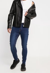 Svart läderbikerjacka med dragkedja fram, kombinerad med slim-fit blå denimjeans och svarta sneakers. Vit t-shirt med rund hals under.
