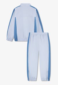 Φωτεινή γαλάζια φόρμα με ζακέτα που κλείνει με φερμουάρ και παντελόνι με ελαστική μέση. Διαθέτει αντίθετες μπλε πλευρικές λωρίδες και λευκό φινίρισμα. Ομαλή υφή.