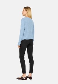 Světle modrý svetr s dlouhými rukávy, v kombinaci s černými slim-fit džíny a tmavě hnědými lakovanými balerínami. Jednoduchý, uvolněný design.