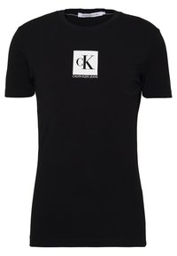 Camiseta negra de algodón con mangas cortas, con un logo cuadrado blanco que muestra "CK" y "CALVIN KLEIN JEANS" impreso debajo.