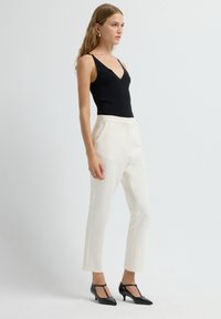 Black sleeveless top with a V-neck, paired with cream tailored trousers and black pointed-toe heels featuring T-strap accents.