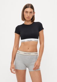 Svart bomulls crop top med korte ermer og hvit Calvin Klein-logo på båndet. Grå bomullsbokser med beige livlinje og svart logodetalj.