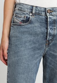 Světle modré džíny z denimu s mírně vybledlým vzhledem, s designem pěti kapes, kovovým knoflíkem a kontrastním prošitím.