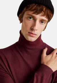 Maglione a collo alto bordeaux con silhouette aderente, texture morbida e dettagli a costine al collo e ai polsini.