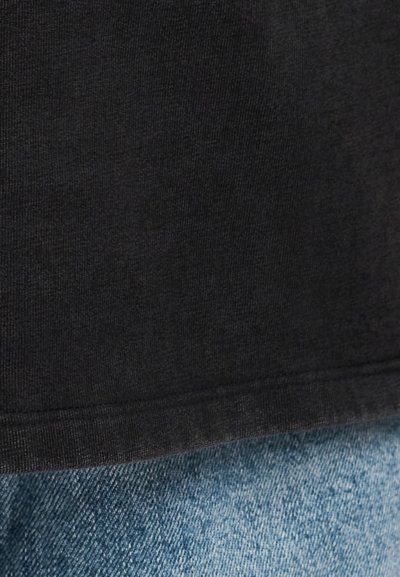 Κοντινό πλάνο του τελειώματος μαύρου υφάσματος πάνω σε ανοιχτό μπλε τζιν ύφασμα, που δείχνει τις λεπτομέρειες υφής και ραφών και στα δύο υλικά.