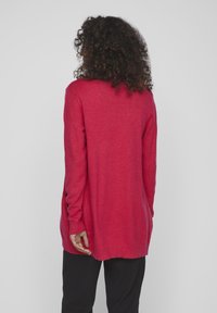 Jersey de punto rojo de manga larga con corte relajado, puños y dobladillo acanalados. Textura suave y detalles de ventilación en la parte posterior.
