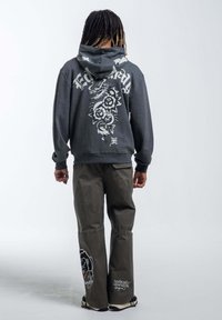 Dark gray hoodie with a graphic design featuring a dragon and roses on the back. Paired with olive green cargo pants with accents.