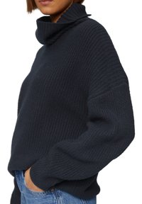 Donkerblauwe, gebreide coltrui met een losse pasvorm. Heeft ribbels aan de mouwen en onderkant, en een structuurafwerking, gecombineerd met lichte denim.