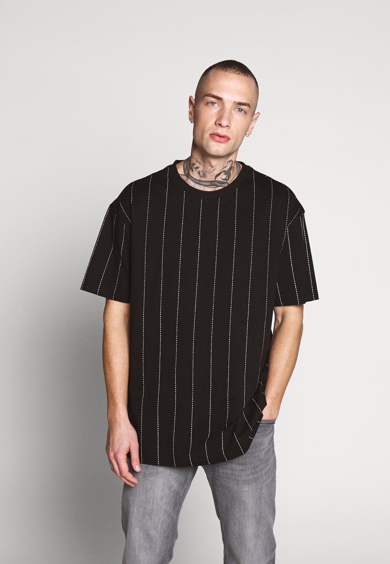 T-shirt noir avec des rayures blanches verticales, coupe décontractée, manches courtes, col rond, avec fentes latérales à l'ourlet.
