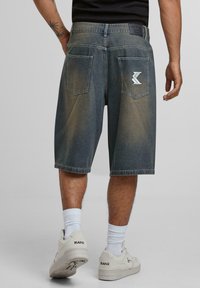 Denim shorts in a faded blue gradient, featuring two back pockets and stitched logo detail. Worn with white sneakers and socks.