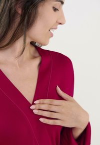 Parte superior de manga corta con escote en V en un vibrante tejido rojo de textura suave. Presenta costuras sutiles y un ajuste relajado, mostrado parcialmente en un modelo.