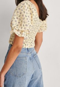 Blouse florale jaune à manches bouffantes et corsage smocké. Associée à un jean en denim bleu clair taille haute avec poches arrière.