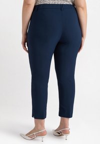 Vyön siniset nilkkahousut, jotka on valmistettu sileästä kankaasta, ja niissä on istuva malli, vyötärökaistale ja halkiot helmassa. Yhdistettynä valkoisiin korkokenkiin.