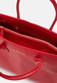 Röd läderväska med krokodilmönster och guldiga detaljer, med en innerficka med dragkedja och två robusta handtag. "Valentino"-logotypen syns.