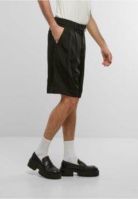 Sorte plisede shorts med belte, sidelommer, skreddersydd passform. Kombinert med hvite sokker og kraftige sorte loafers. Myk tekstur.