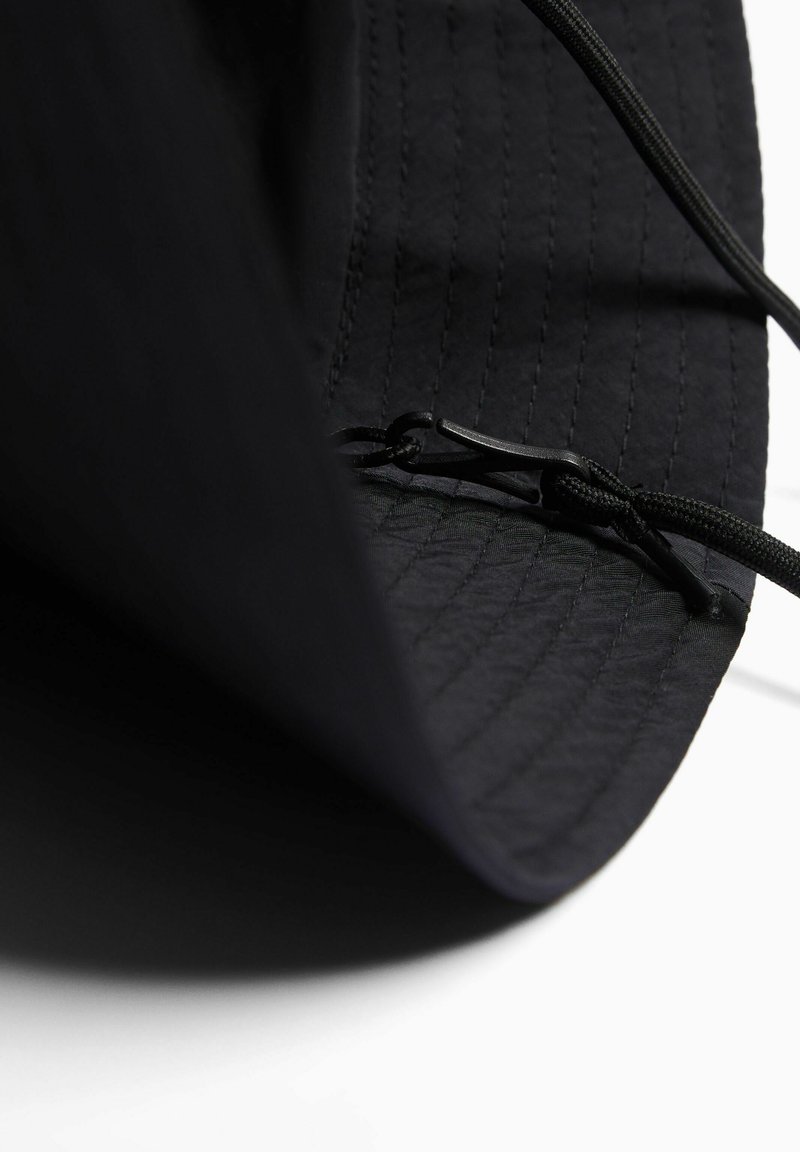 Sombrero negro hecho de tela texturizada, con un ala moldeada y un cordón ajustable en el interior para un ajuste seguro. Detalles de costura visibles.