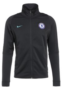 Veste de sport noire zippée avec le logo de Chelsea FC sur la poitrine gauche et le swoosh Nike bleu clair sur la poitrine droite, manches longues et col montant.
