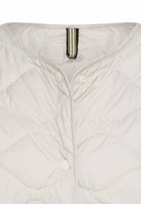 Veste matelassée blanche avec un col arrondi, dotée de deux boutons-pression et d'une boucle en tissu rayé au niveau du cou. Texture douce et lisse.