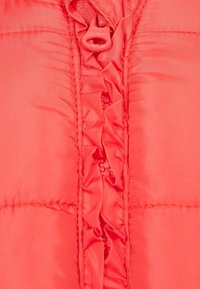 Koraal kleurige pufferjack met een ritssluiting aan de voorkant, geplooide ruffles langs de opening en een gladde, lichte stof.