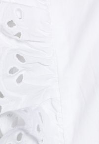 Weißer Stoffabschnitt mit rüschengeschnittenem Rand, bestickten Ausschnitten, glatter Textur und aufwendiger Detailarbeit am Saum.