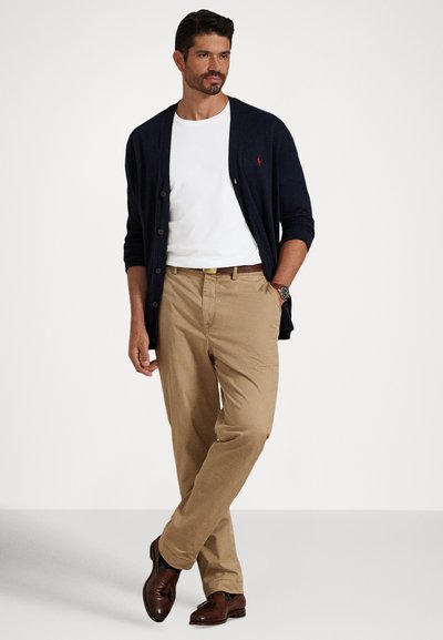 Marinblå cardigan, vit t-shirt, khakifärgade byxor, brunt skärp och bruna skor. Cardigan har knappar; byxorna är rakskurna och har fickor.