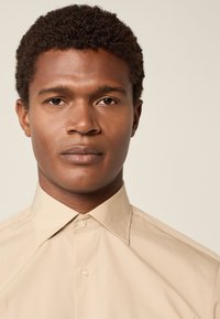 Béžová košile na knoflíky s klasickým límcem, vyrobená z hladké látky, s předním límcem a malými kulatými knoflíky.