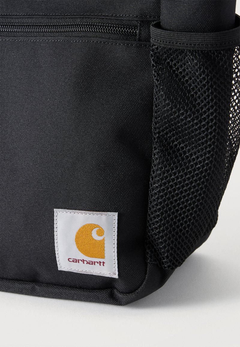 Borsa in tessuto nero con tasca frontale con zip, tasca laterale in rete e patch cucito con logo Carhartt bianco in giallo e rosso.