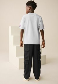 Hellgraues T-Shirt mit kurzen Ärmeln und gesticktem Design auf dem Ärmel, kombiniert mit schwarzen Cargo-Hosen mit mehreren Taschen.