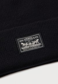 Musta neulottu kangas suorakulmaisen Levi Strauss & Co. -tunnuksen kanssa, jossa kaksi hevosta vetää erilleen farkkuja.