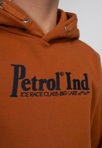 Oranje hoodie van zacht materiaal, met een capuchon met trekkoord en donkerblauwe geborduurde tekst: "Petrol Ind Ice Race Class-Big Lake."