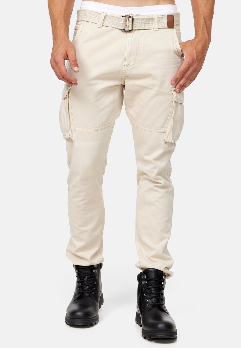 Beige Cargo-Hosen mit einer figurschmeichelnden Silhouette, mehreren Seitentaschen, genähten Details und einem passenden Gürtel. Getragen mit schwarzen Kampfstiefeln.