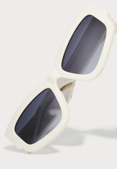 White oversized sunglasses with dark tinted lenses, featuring a thick frame and angular design. Smooth texture with visible logo on inside.