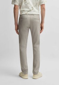 Ljust grå byxor i texturerad tyg, slim fit design, två bakfickor, kombinerat med krämfärgade sneakers. Minimalistisk och modern framtoning.