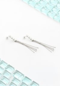 Silver hängande örhängen med sfäriska pärl-inlägg och flera delikata kedjor, visade på en vit bakgrund med glasblock.