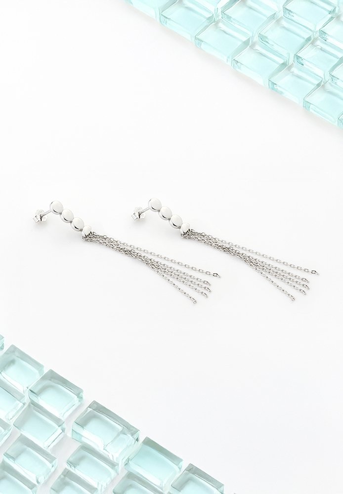 Silver hängande örhängen med sfäriska pärl-inlägg och flera delikata kedjor, visade på en vit bakgrund med glasblock.