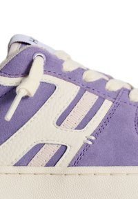 Sneaker in suede viola con accenti crema, dotato di lacci piatti, suola in gomma e finitura testurizzata. Il design notevole include dettagli ritagliati.