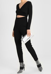 Body de manga larga negro con detalles recortados, combinado con pantalones negros ajustados. Clutch metálico plateado y botas de tacón brillantes plateadas.