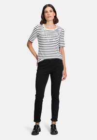 Striped short-sleeve t-shirt in white and navy, featuring a round neckline and front graphic. Paired with black slim-fit pants and black shoes.