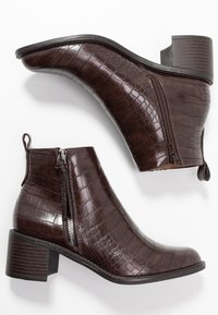 Botas de tobillo de imitación de cocodrilo en color marrón, con tacón cuadrado, que cuentan con cierres de cremallera y una superficie texturizada para mayor detalle.