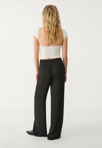 Bílý krátký top s krátkými rukávy, spárovaný s volnými, černými, nohavicemi s vysokým pasem a strukturovaným povrchem. Černé boty s akcenty.