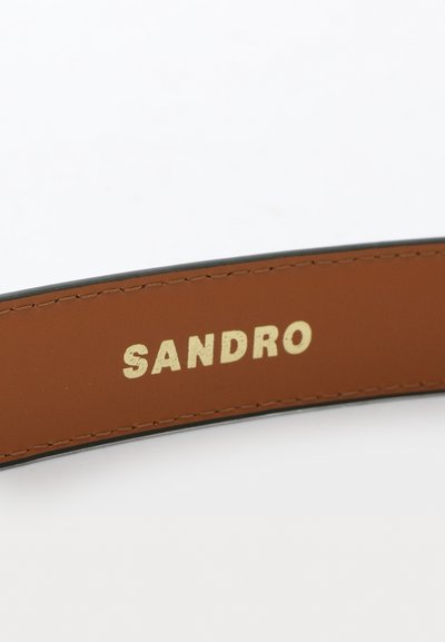 Pruun nahk vöö, millel on sile tekstuur, millel on kuldne reljeefne "SANDRO" logo, tikandid servade ümber ja must äär.