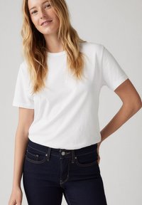 Camiseta blanca de manga corta con cuello redondo, combinada con unos vaqueros azul oscuro con costuras contrastantes y bolsillos delanteros.