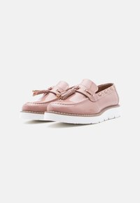 Mocassins rose blush brillants avec des glands et des semelles blanches, présentant des détails cousus et des œillets dorés sur un fond blanc uni.