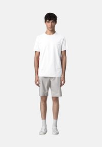 T-shirt bianca in cotone con taschino, abbinata a pantaloni corti grigio chiaro. Modello che indossa sneakers bianche e calzini bianchi a lunghezza crew.